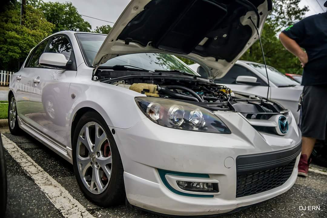 White first-generation Mazda3 with its hood open, viewed from the front quarter.