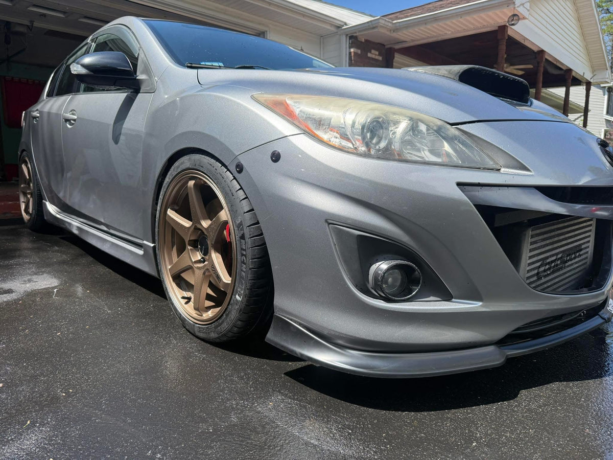 Silver second-generation Mazdaspeed3 showing two black latches along the bumper-to-fender seam.