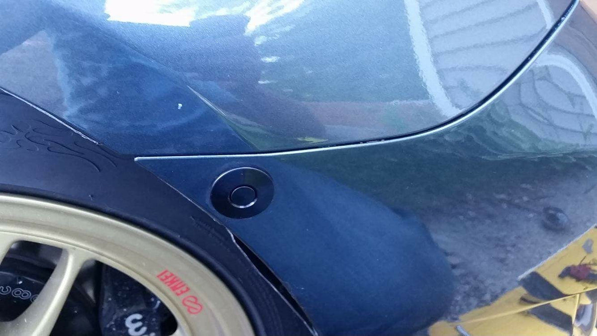 Black quick-release latch mounted at the wheel-arch end of a dark blue bumper.