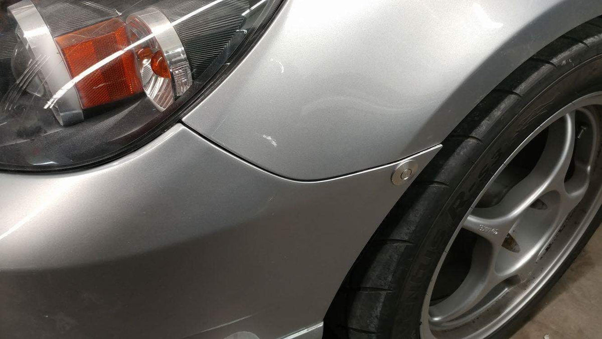 Silver latch installed near the front wheel arch of a silver first-generation Mazda3.