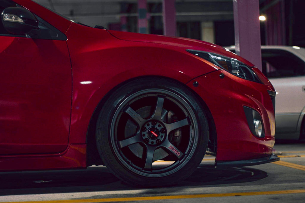 Side view of a red second-generation Mazdaspeed3 showing black latches along the front bumper seam.