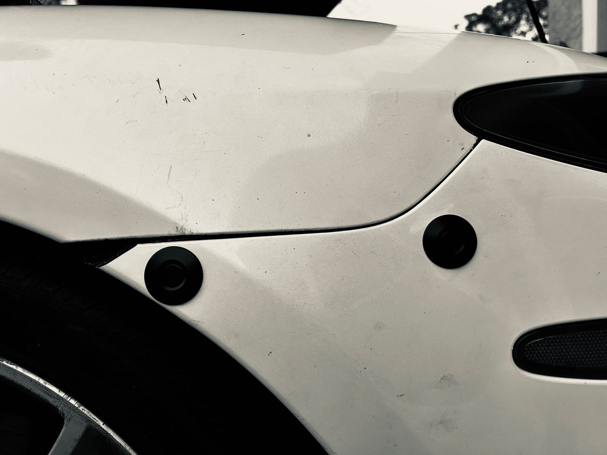 Two black quick-release latches mounted below the bumper-to-fender seam on a white car.