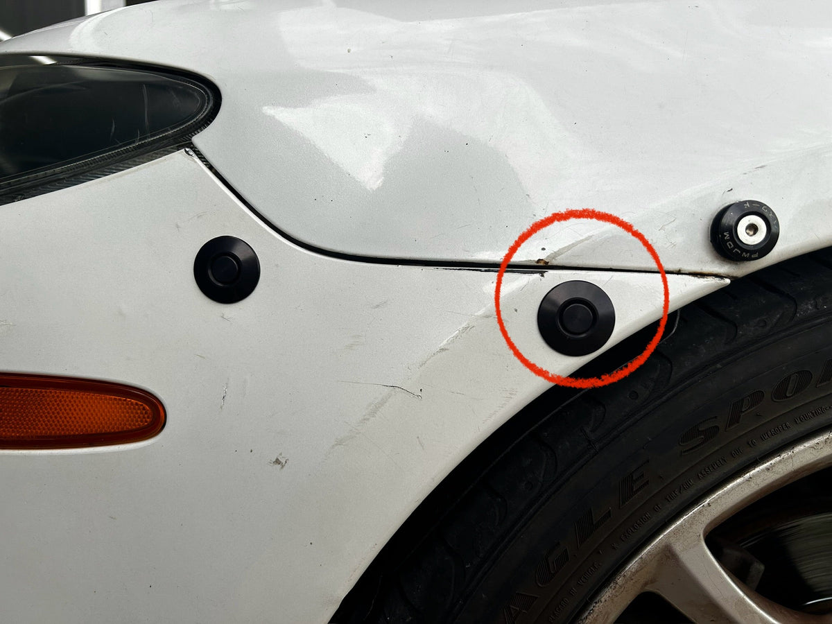 White bumper closeup with the wheel-arch latch circled and a second latch closer to the headlamp.