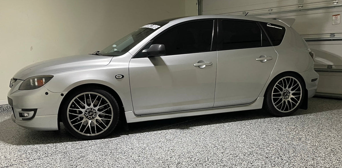 Side view of a silver first-generation Mazdaspeed3 with bumper latches, parked in a garage.