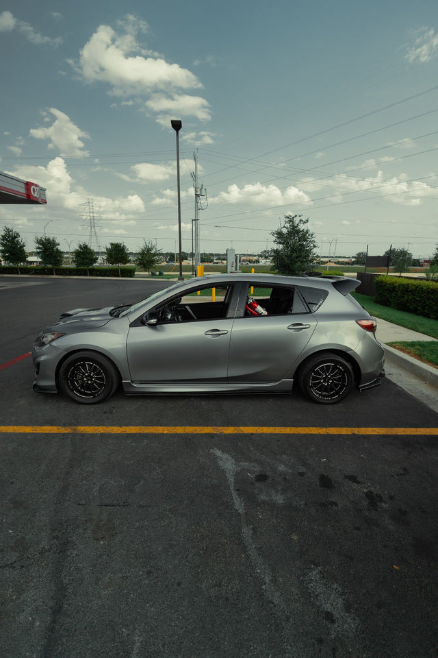 Side profile of the silver Mazdaspeed3 parked with its hood open.